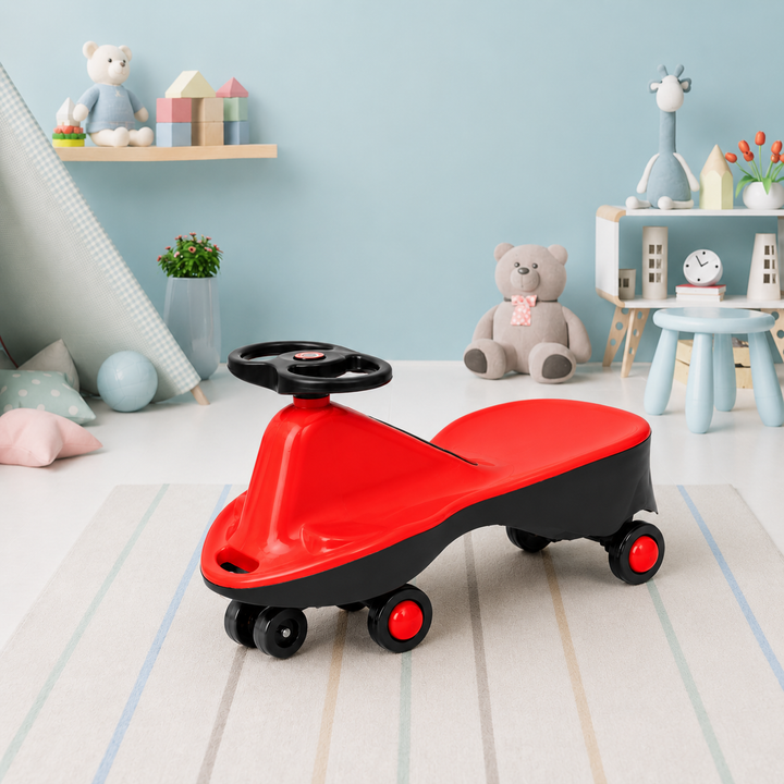A red and black plastic children's ride-on toy car with a steering wheel and four wheels, shown in a styled children's room setting with toys and furniture in the background.