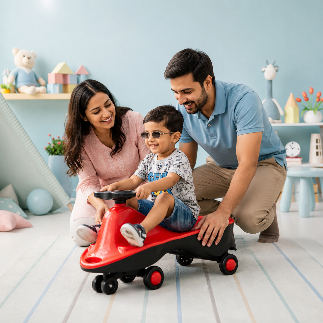 A young boy wearing sunglasses sits on a red and black ride-on toy car while his father and mother smile and assist him in a brightly lit children's playroom.