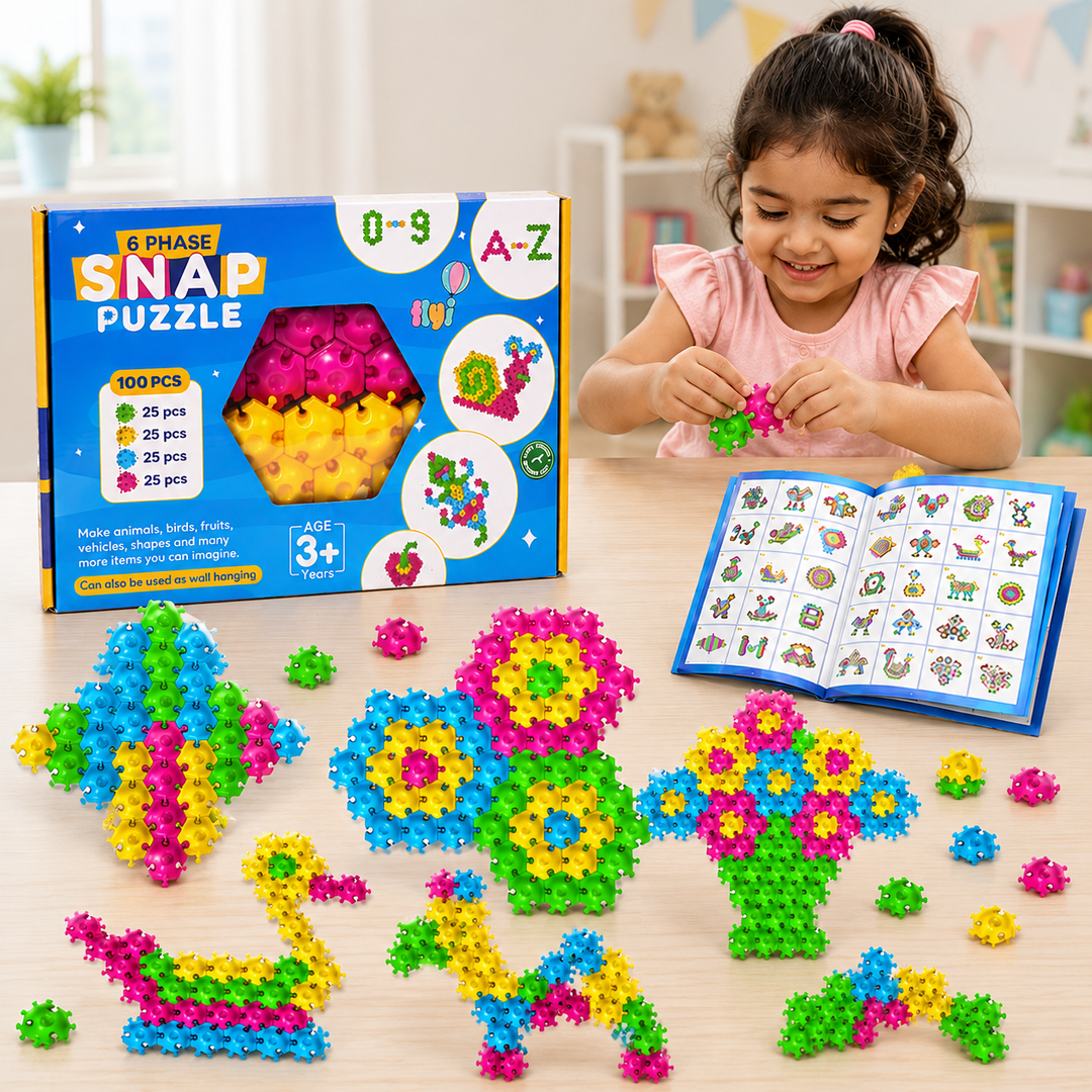 A young girl in a pink shirt is sitting at a light wood table, smiling while building with colorful plastic snap puzzle pieces. In front of her is an open book showing animal and nature illustrations, and several colorful geometric structures are arranged on the table.